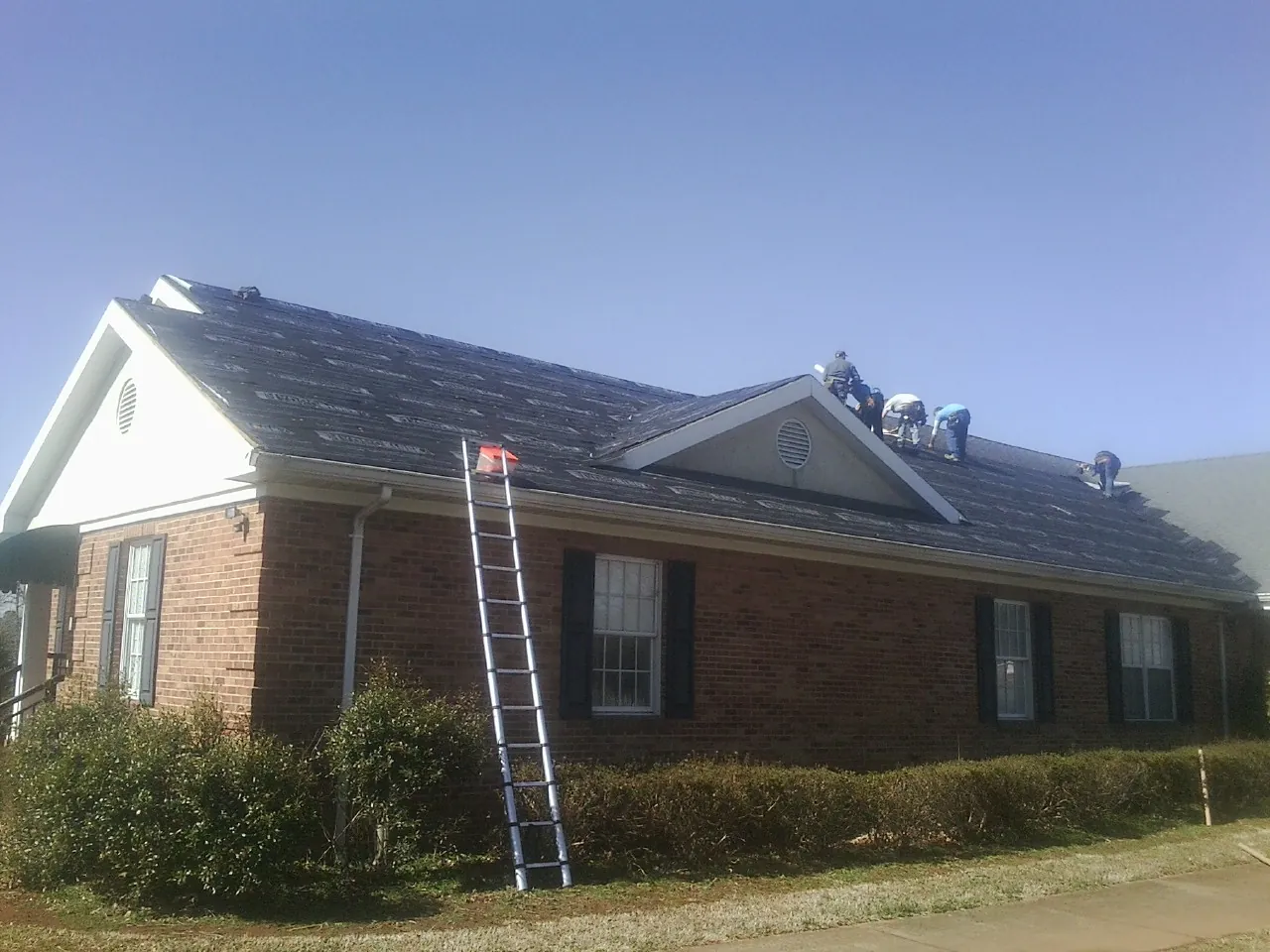 Crew tearing shingles off a brick ranch roof with a ladder set — Emergency Roof Repair work by our crew in Gettysburg