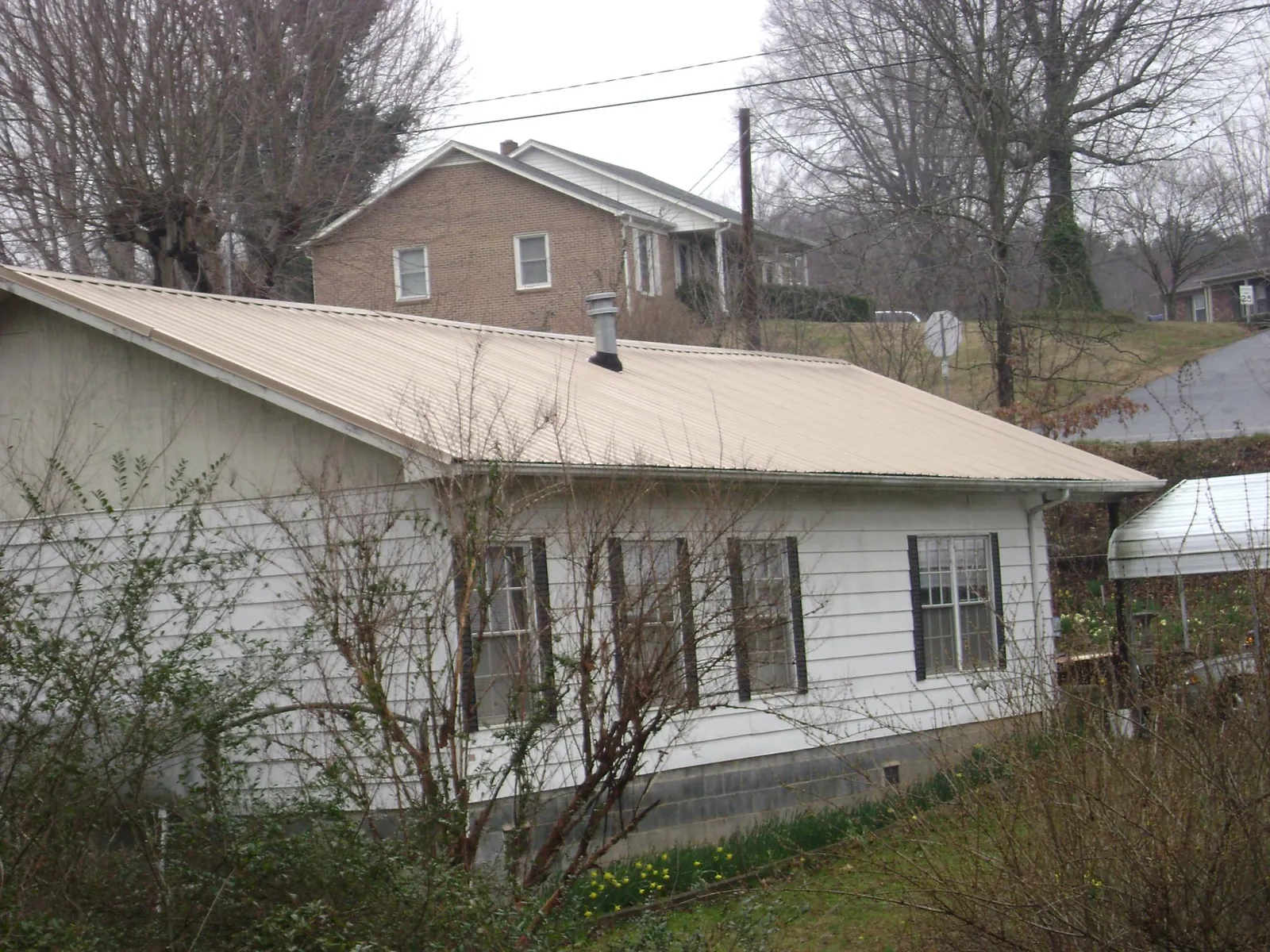 Tan metal roof on a white sided house set into a hillside — Commercial Roofing by Roofing Brothers in Gettysburg